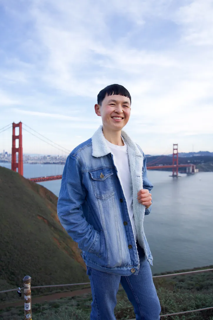 Man in a denim jacket smiling with the Golden Gate Bridge behind him