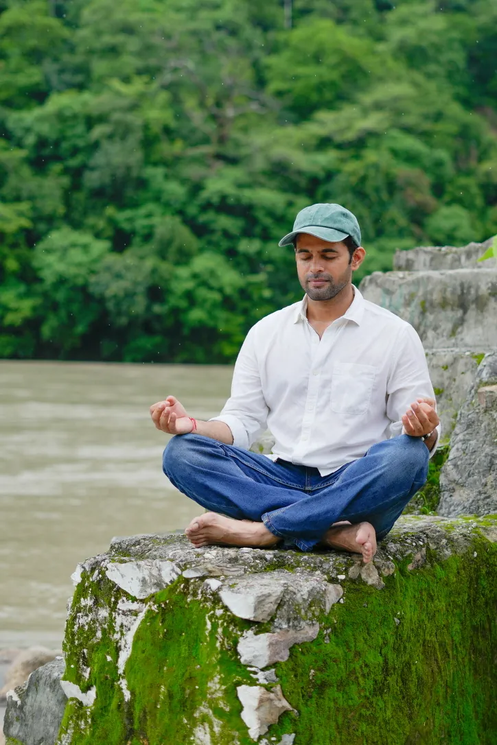 Man meditating cross-legged on a rock by a river