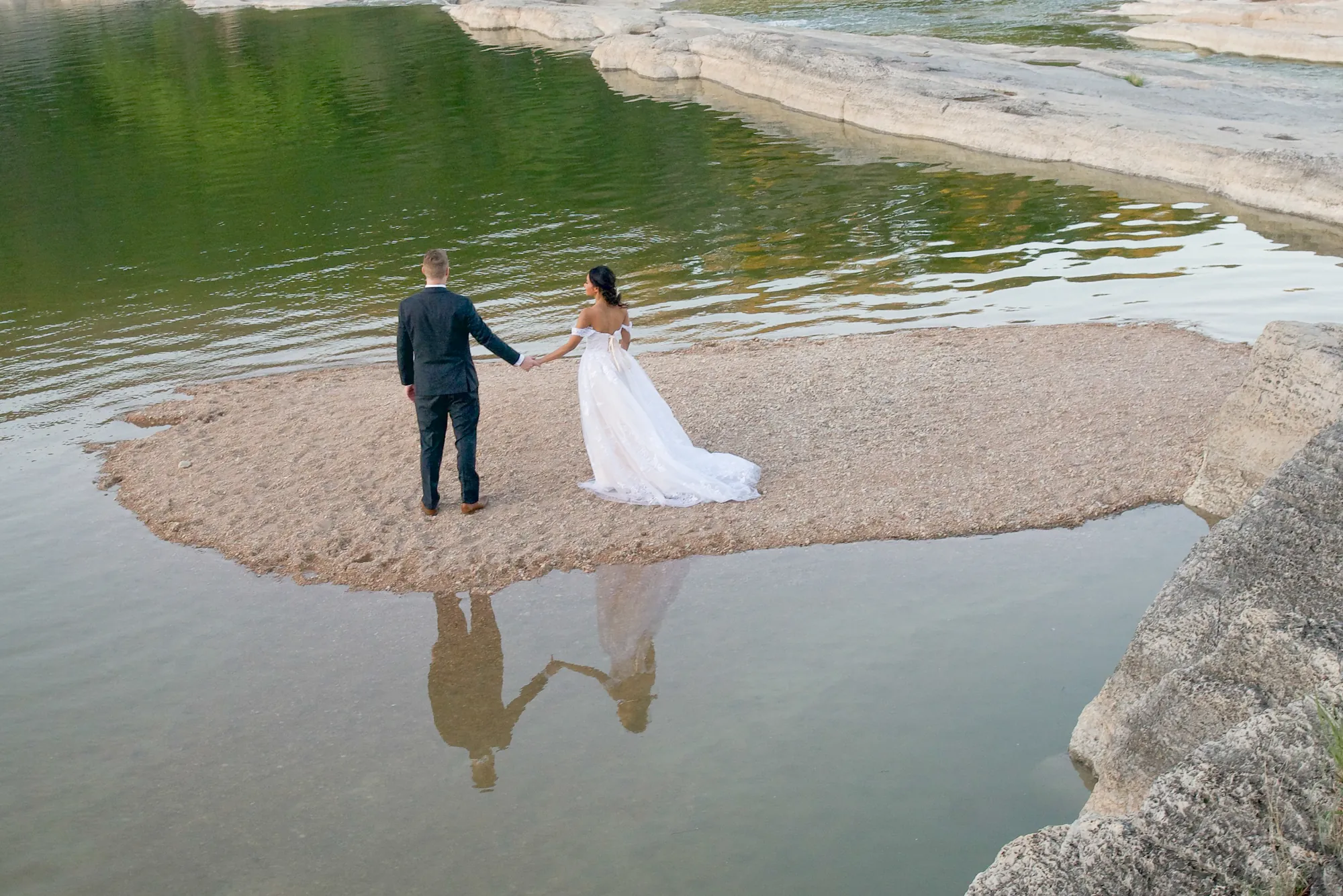 Couple in wedding attire standing on a sandbar in a river