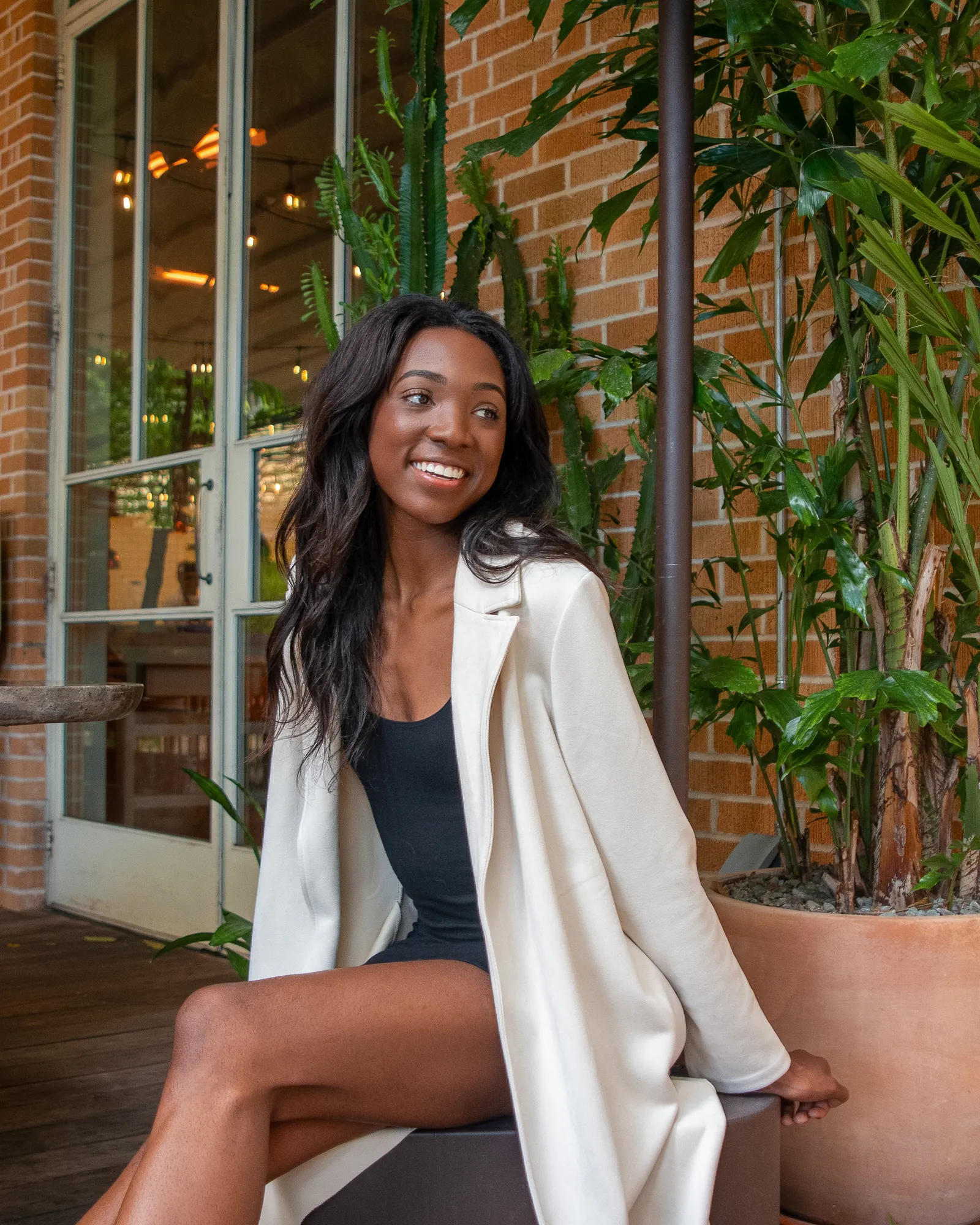 Smiling woman in a cream coat seated outside a brick café